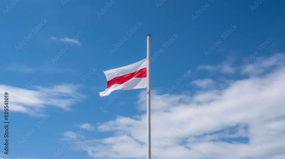 A flag with a red and white pattern flutters proudly against a bright blue sky.