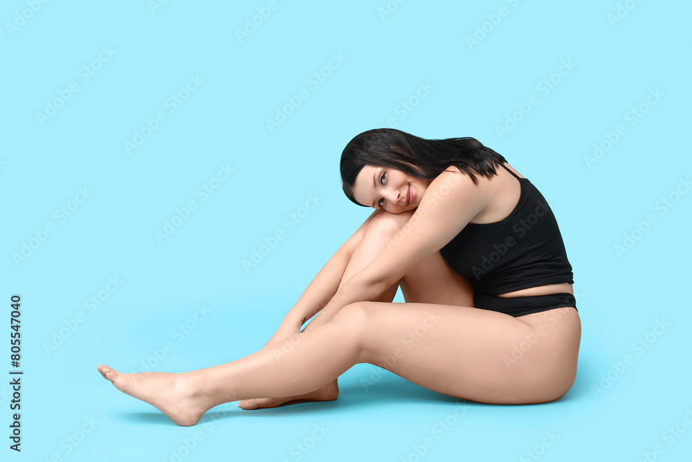 Body positive young woman in underwear sitting on blue background Body positive young woman in underwear sitting on blue background