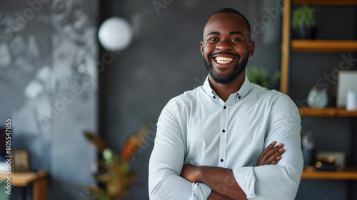 Happy handsome young African American entrepreneur man in office shirt standing indoors with crossed arms  looking at camera with toothy smile  laughing. Business professional vertical portrait