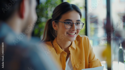 Happy young job candidate woman in informal clothes talking to employee on interview, talking to boss with toothy smile, meeting with colleague at work table, discussing paper resume