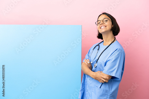 Young mixed race surgeon woman with a big banner over isolated background with arms crossed and looking forward photo
