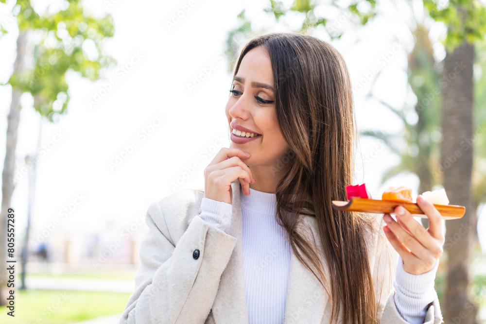 Young pretty woman holding sashimi at outdoors thinking an idea and looking side Young pretty woman holding sashimi at outdoors thinking an idea and looking side