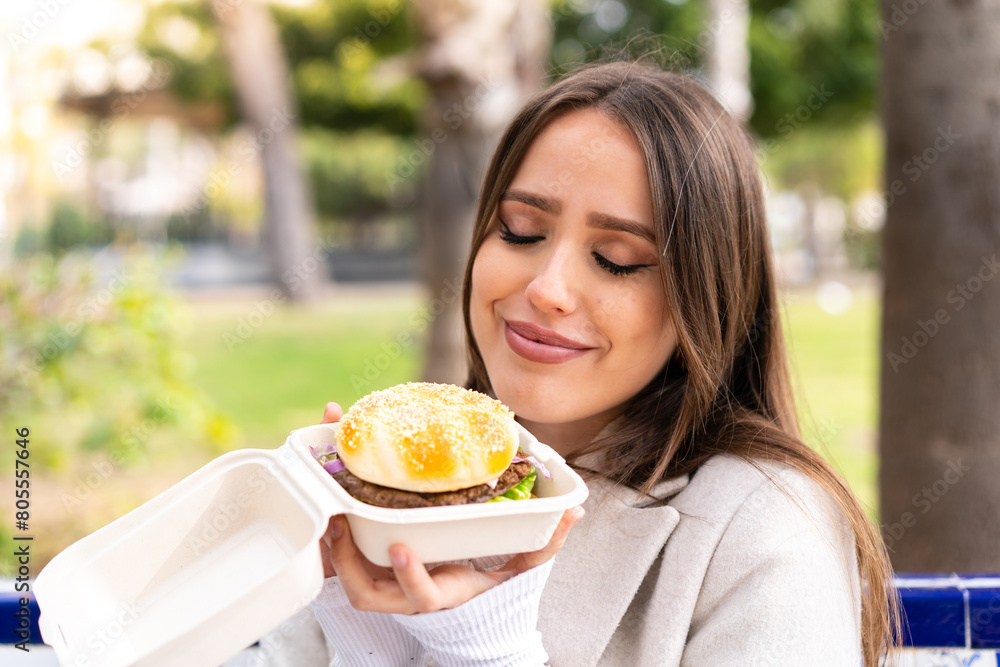Young pretty woman holding a burger at outdoors Young pretty woman holding a burger at outdoors