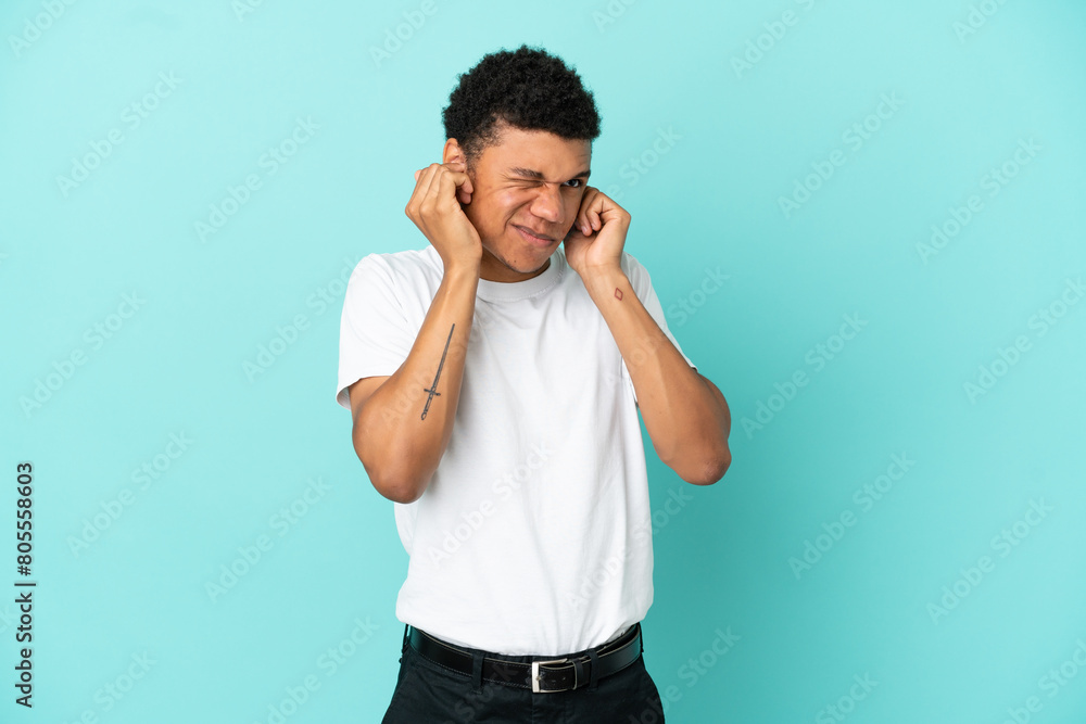 Young African American man isolated on blue background frustrated and covering ears Young African American man isolated on blue background frustrated and covering ears