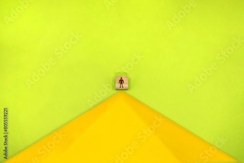 黄色い山のてっぺんに人のシルエットマークのブロックが立つ緑色の背景 photo