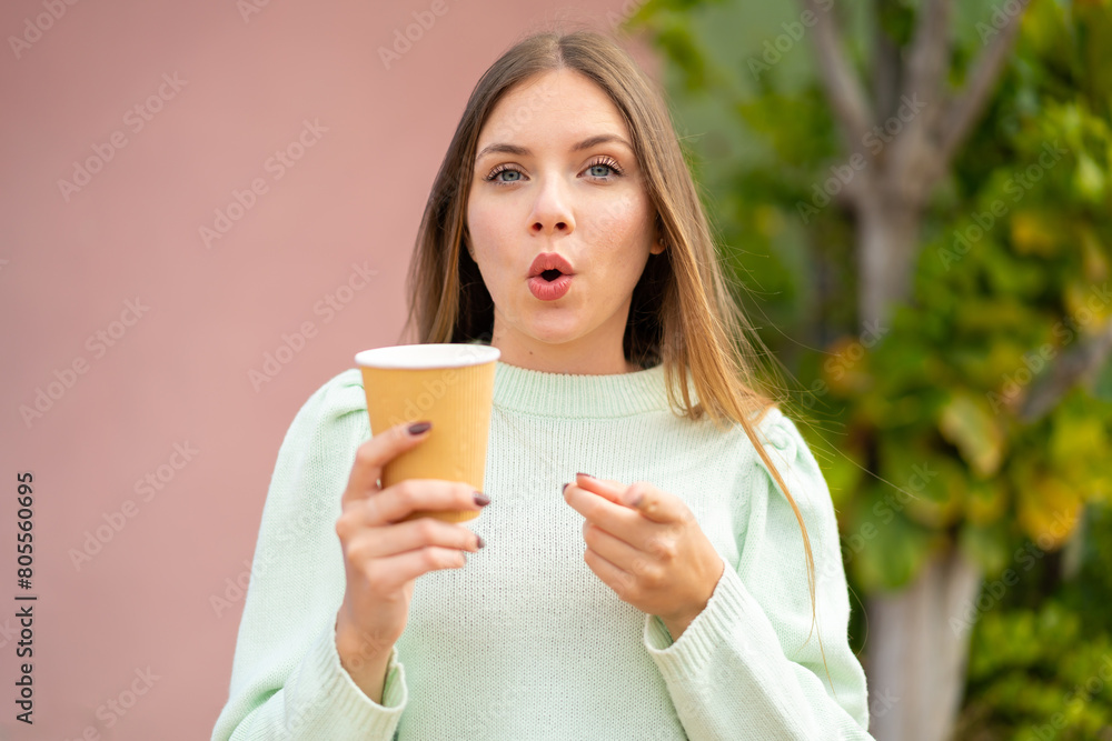 Young pretty blonde woman holding a take away coffee at outdoors surprised and pointing front Young pretty blonde woman holding a take away coffee at outdoors surprised and pointing front