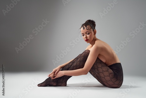 Sensual topless woman embracing herself and sitting on floor