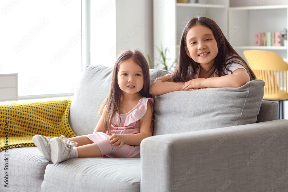 Cute little Asian happy sisters sitting on sofa at home Cute little Asian happy sisters sitting on sofa at home