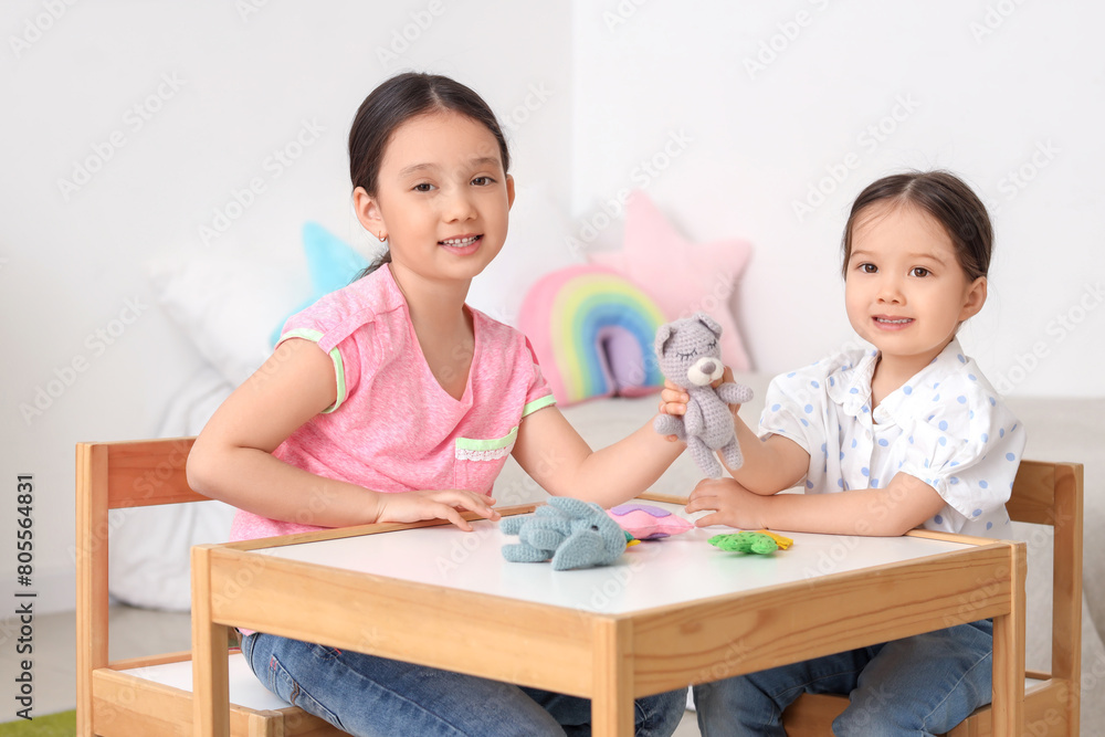 Cute little Asian happy sisters playing with cuddly toys at table in child room Cute little Asian happy sisters playing with cuddly toys at table in child room