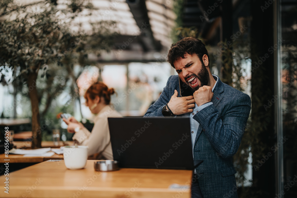 Focused businessman working on a laptop at a busy cafe with a businesswoman in the backdrop Focused businessman working on a laptop at a busy cafe with a businesswoman in the backdrop