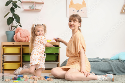 Nanny with little girl putting toys away at home
