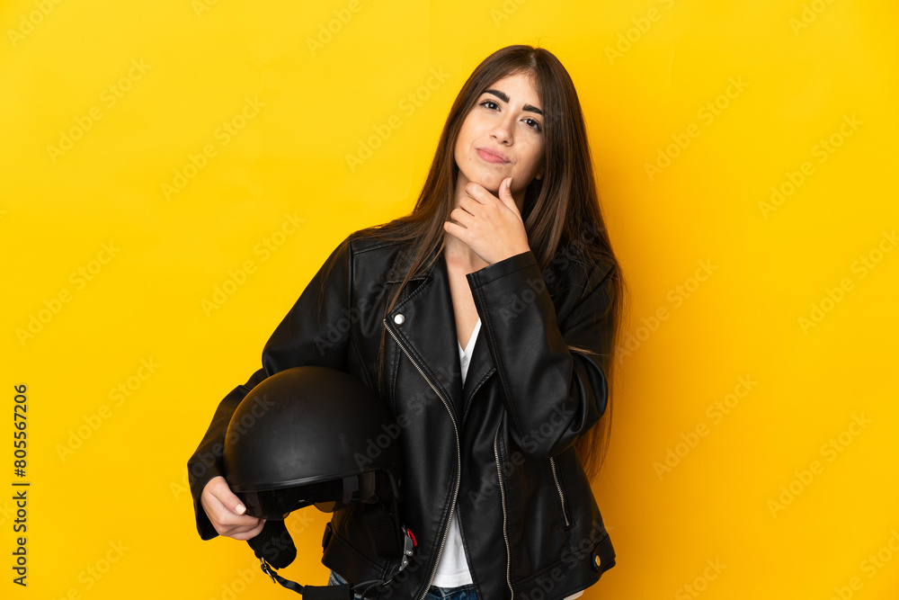 Young caucasian woman holding a motorcycle helmet isolated on yellow background and looking up Young caucasian woman holding a motorcycle helmet isolated on yellow background and looking up