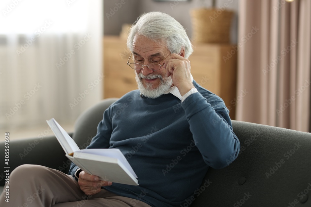 Portrait of happy grandpa reading book on sofa indoors Portrait of happy grandpa reading book on sofa indoors