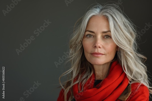 A stylish woman with silver-gray hair stands out against a gray background wearing a vibrant red scarf and a serene expression photo