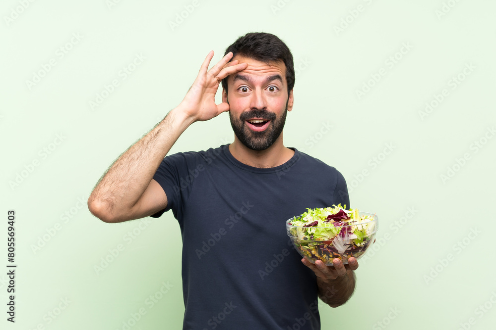 Young handsome man with salad over isolated green wall has just realized something and has intending the solution
