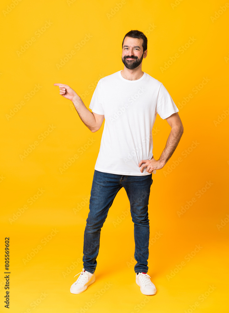 Full-length shot of man with beard over isolated yellow background pointing finger to the side Full-length shot of man with beard over isolated yellow background pointing finger to the side