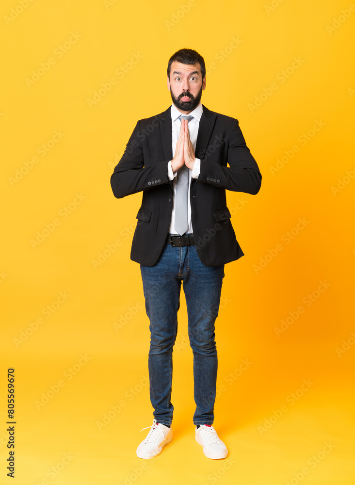 Full-length shot of business man over isolated yellow background keeps palm together. Person asks for something Full-length shot of business man over isolated yellow background keeps palm together. Person asks for something