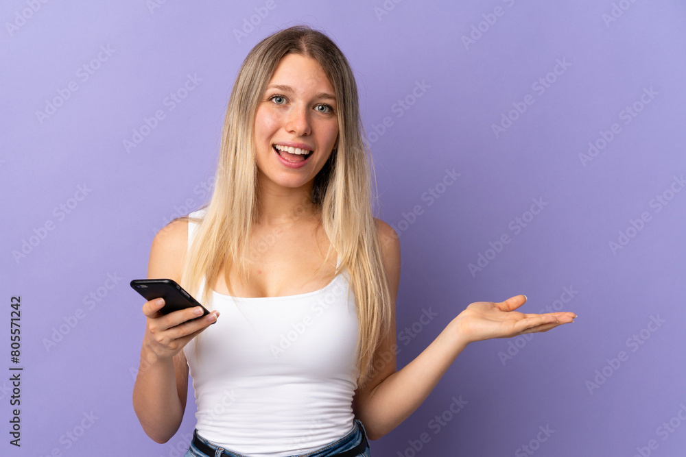 Young blonde woman using mobile phone isolated on purple background extending hands to the side for inviting to come Young blonde woman using mobile phone isolated on purple background extending hands to the side for inviting to come