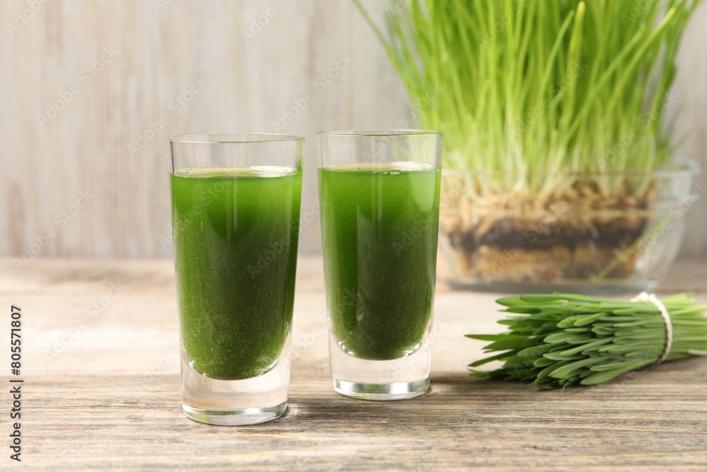 Wheat grass drink in shot glasses and fresh green sprouts on wooden table, closeup Wheat grass drink in shot glasses and fresh green sprouts on wooden table, closeup