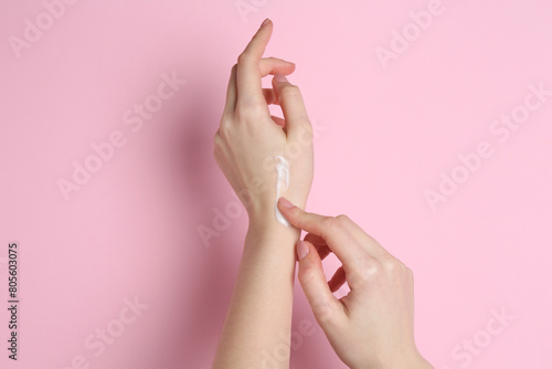 Woman applying cream on her hand against pink background, closeup © New Africa