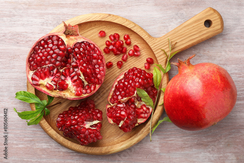 Fresh pomegranates and green leaves on wooden table, top view