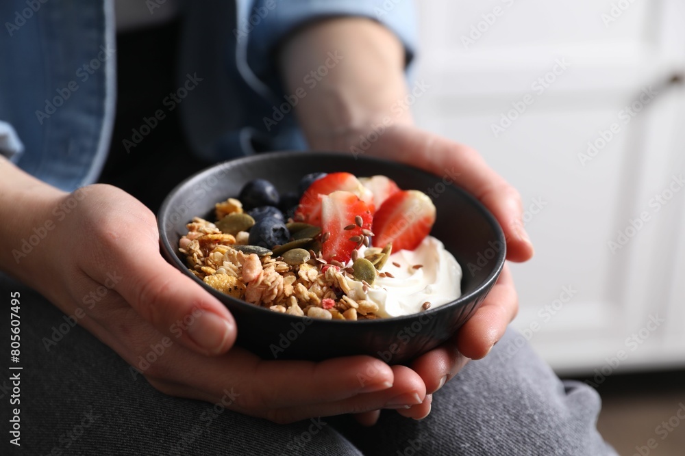 Woman holding bowl of tasty granola with berries, yogurt and seeds indoors, closeup Woman holding bowl of tasty granola with berries, yogurt and seeds indoors, closeup
