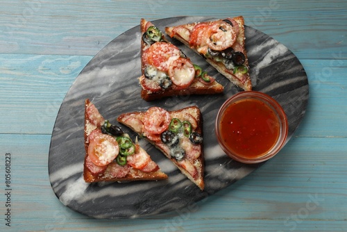 Tasty pizza toasts and sauce on light blue wooden table, top view