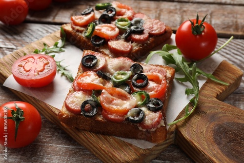 Tasty pizza toasts, tomatoes and arugula on wooden table, closeup