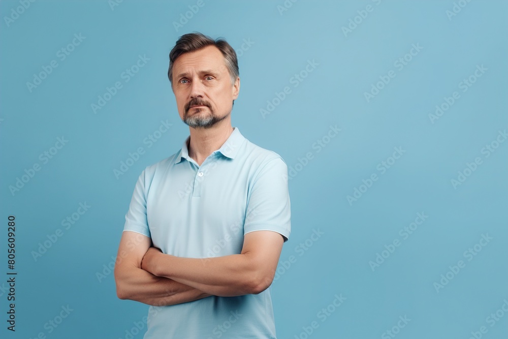 A man in a blue shirt is standing with his arms crossed and looking away A man in a blue shirt is standing with his arms crossed and looking away