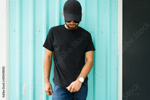 Mockup and casual wear design: hispanic man wearing a black t-shirt and cap against a turquoise background