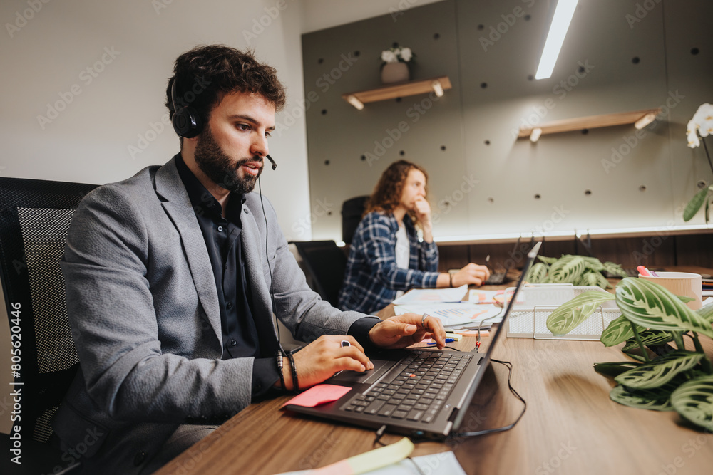 A man and woman working diligently in an office setting, focused on their tasks with computers and office accessories. A man and woman working diligently in an office setting, focused on their tasks with computers and office accessories.