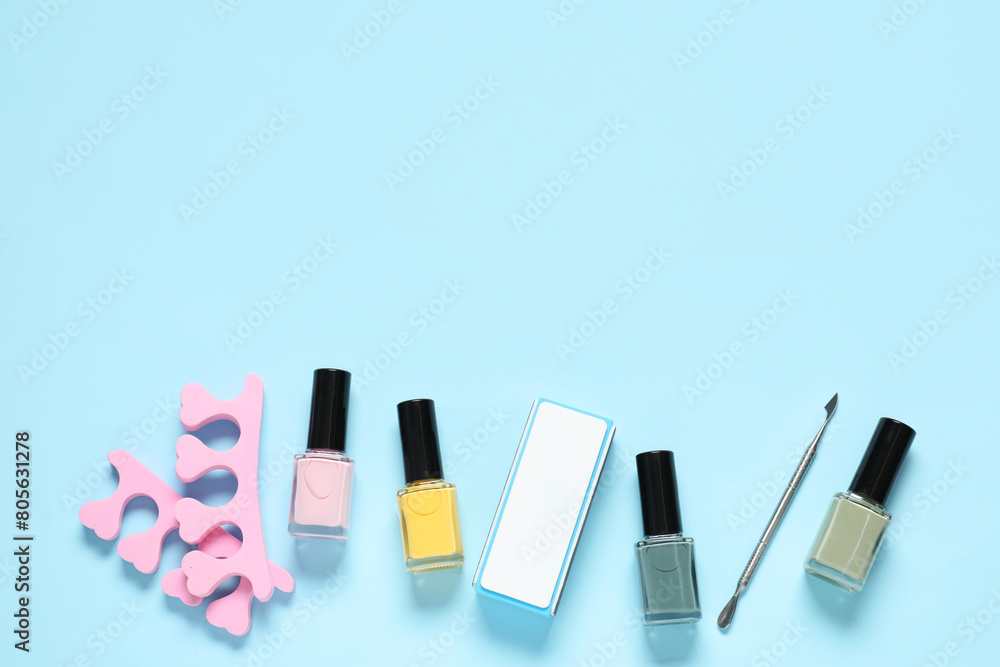 Nail polishes, toe separators, buffer and cuticle pusher on light blue background, flat lay. Space for text Nail polishes, toe separators, buffer and cuticle pusher on light blue background, flat lay. Space for text