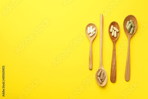 Different vitamin capsules in spoons on yellow background  flat lay. Space for text