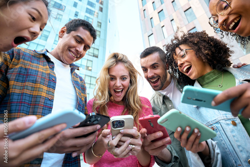 Low angle view of a group of young jaw dropping mixed race people with mobile phones. Excited students using their technological devices. Concept of enterprising, friendly, app, hipster, millennial