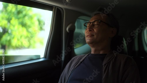Relaxing moment of Senior old man sitting in car back seats using smartphone play social media with safety belt and look out the window. Grandfather happy in car traveling on the road to destination.
