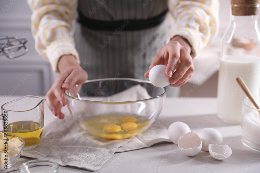 Making dough. Woman breaking egg at white table in kitchen, closeup Making dough. Woman breaking egg at white table in kitchen, closeup