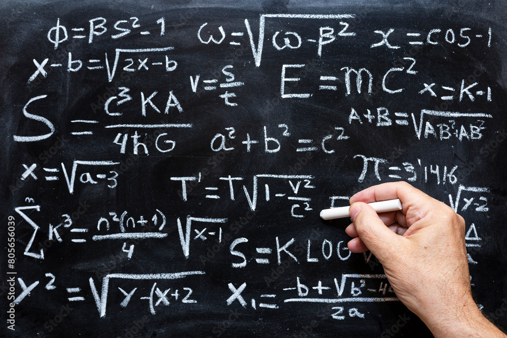 Mano escribiendo operaciones matemáticas y formulas de física cuántica con una tiza en la pizarra Mano escribiendo operaciones matemáticas y formulas de física cuántica con una tiza en la pizarra