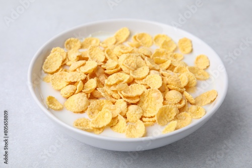 Breakfast cereal. Corn flakes and milk in bowl on light grey table, closeup