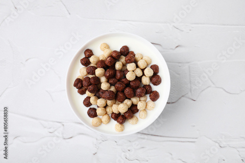 Breakfast cereal. Tasty corn balls with milk in bowl on white textured table, top view