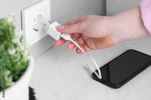 Cuadro en lienzo Woman plugging smartphone into power socket at white table indoors, closeup