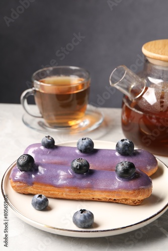 Tasty glazed eclair with blueberries and tea on grey marble table, closeup