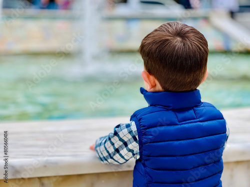 Little boy stands in front of a fountain against a cloudy day