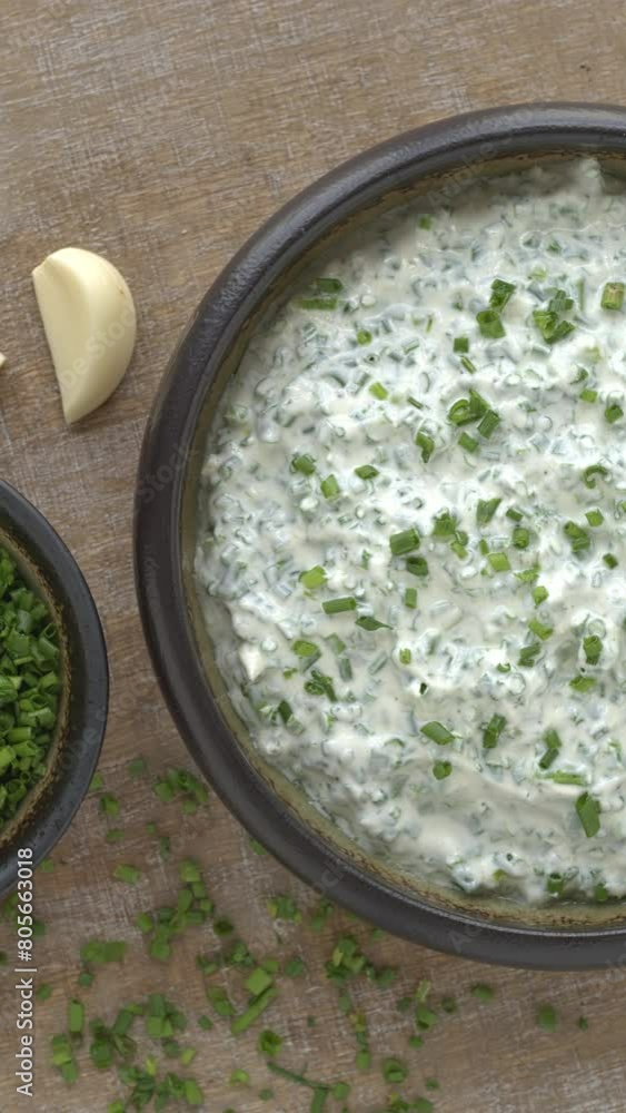 Homemade Greek Yogurt Chive dip in a clay bowl. A second bowl with chopped chives and garlic cloves on the side. Table spin; vertical video. Homemade Greek Yogurt Chive dip in a clay bowl. A second bowl with chopped chives and garlic cloves on the side. Table spin; vertical video.
