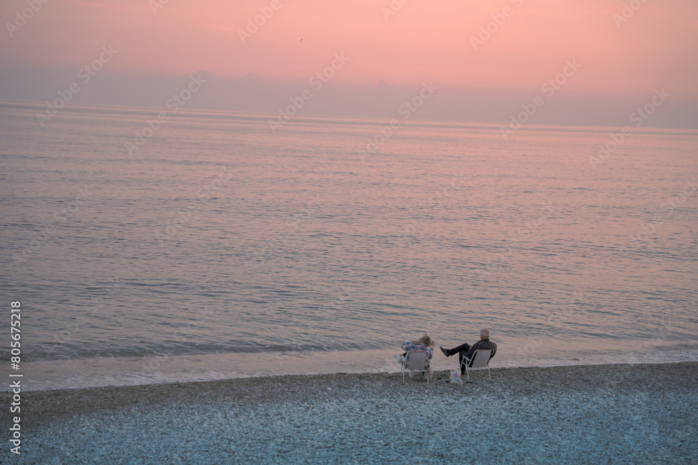 Old pair sitting on the beach looking at sunset Old pair sitting on the beach looking at sunset