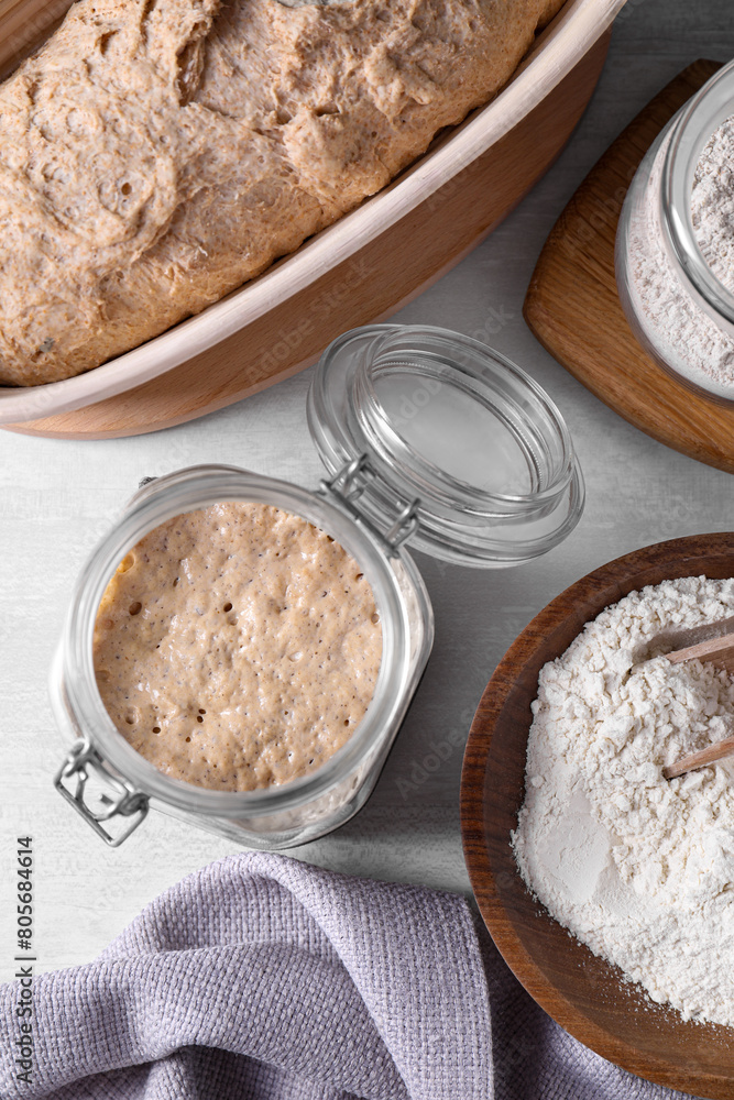 Sourdough starter in glass jar, flour and dough on light table, flat lay Sourdough starter in glass jar, flour and dough on light table, flat lay