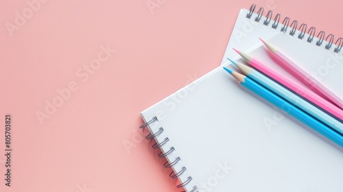 Open blank white notebook accompanied by light blue, pink, and white colored pencils on pastel pink backdrop. Ai Generated