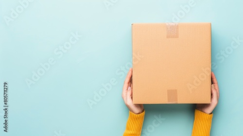 From a top view, a female hand holds a brown cardboard box against a light blue background, Ai Generated. © Crazy Juke