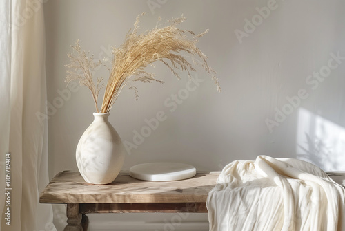 Modern white ceramic vase with dry Lagurus ovatus grass and marble tray on vintage wooden bench  table. Blurred beige linen blanket in front. Scandinavian interior. Empty white wall  copy space