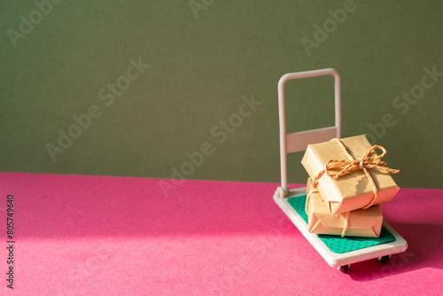 Obraz na płótnie Trolley cart with gift boxes on pink and khaki green background. Parcel Delivery Concept w salonie