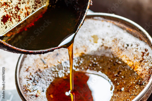 Pouring used cooking oil from frying pan into colander.